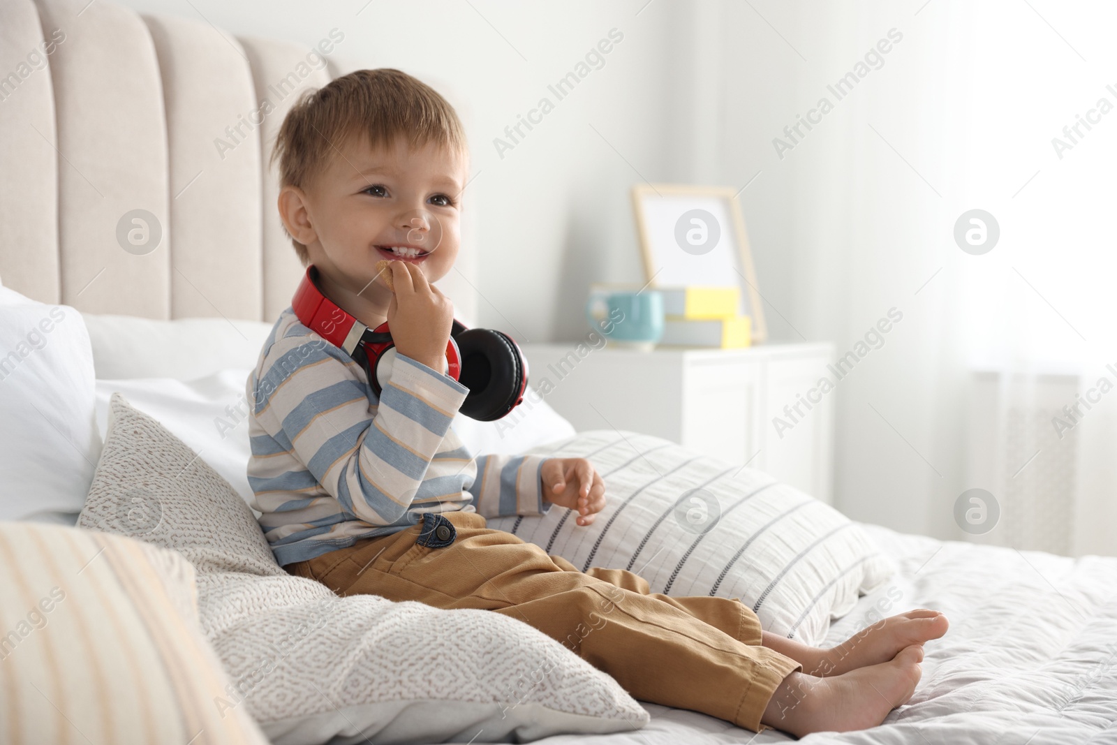 Photo of Cute little baby with headphones on bed at home