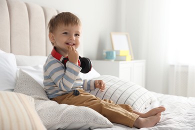 Cute little baby with headphones on bed at home