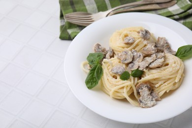 Photo of Delicious pasta with mushrooms and basil served on white tiled table, closeup. Space for text