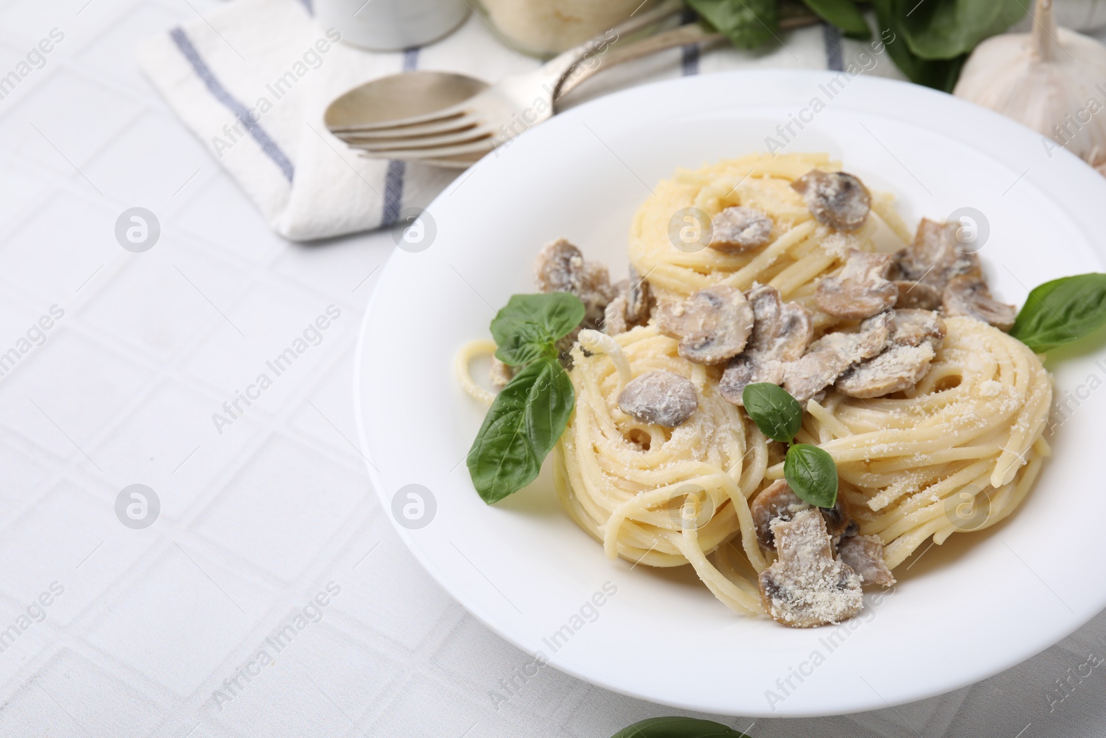 Photo of Delicious pasta with mushrooms and basil on white tiled table, closeup. Space for text