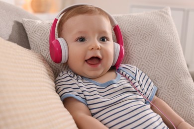 Photo of Cute little baby with headphones on sofa at home