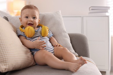 Cute little baby with headphones on sofa at home, space for text