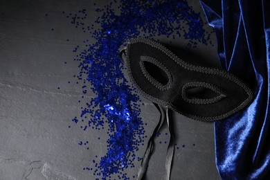 Beautiful carnival mask and blue sequins on black table. Space for text