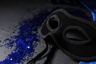 Photo of Beautiful carnival mask and blue sequins on black table, closeup