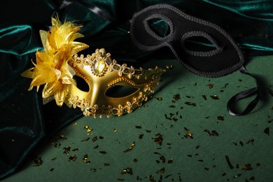 Photo of Beautiful golden carnival masks and silk fabric on green background, closeup