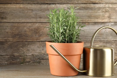 Photo of Aromatic rosemary plant in pot and watering can on wooden table, space for text