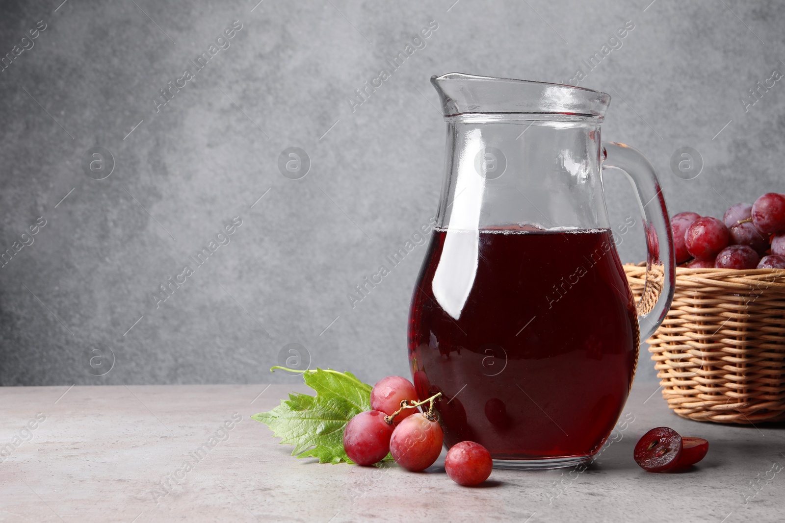 Photo of Ripe grapes and jug of tasty juice on grey table. Space for text