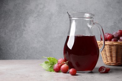 Photo of Ripe grapes and jug of tasty juice on grey table. Space for text