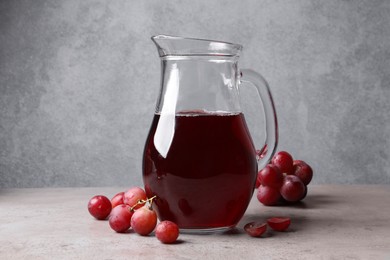 Ripe grapes and jug of tasty juice on grey table