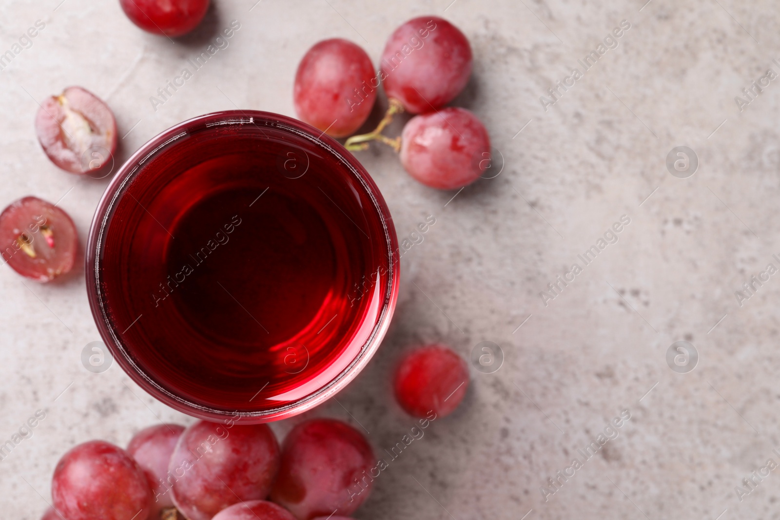 Photo of Ripe grapes and glass of tasty juice on grey table, flat lay. Space for text