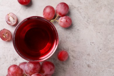 Ripe grapes and glass of tasty juice on grey table, flat lay. Space for text