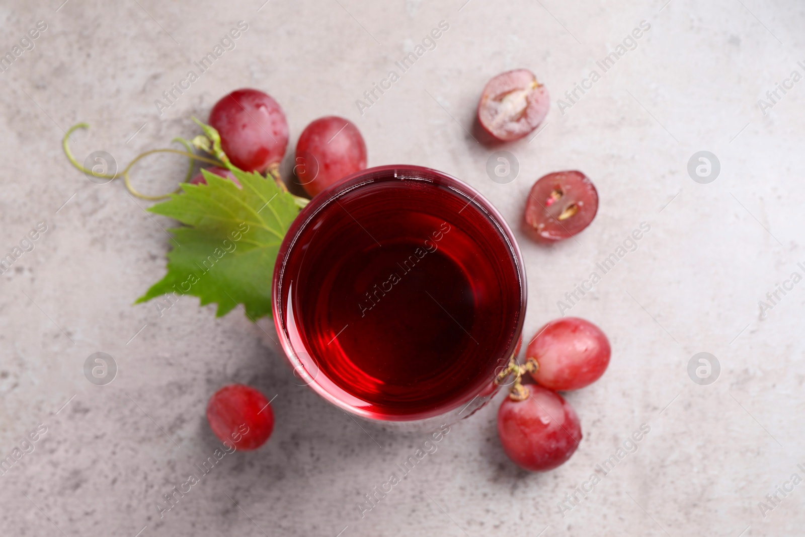 Photo of Ripe grapes and glass of tasty juice on grey table, flat lay