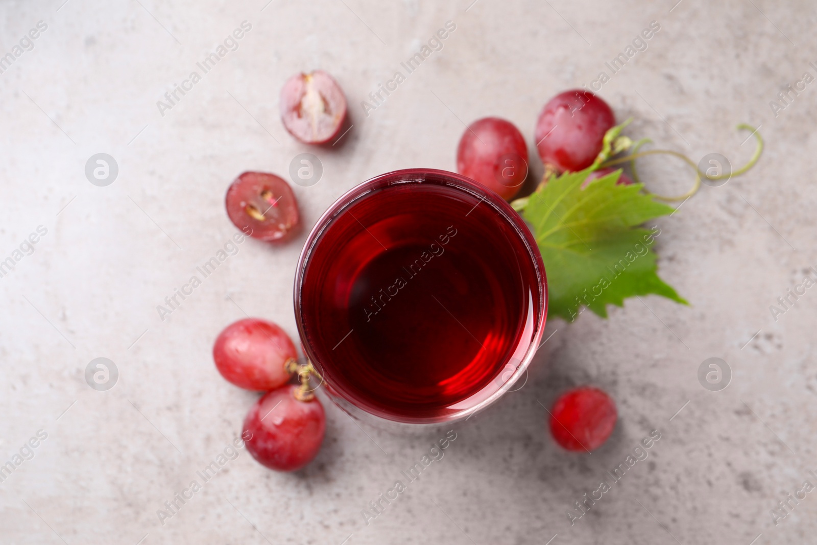 Photo of Ripe grapes and glass of tasty juice on grey table, flat lay