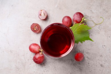 Photo of Ripe grapes and glass of tasty juice on grey table, flat lay