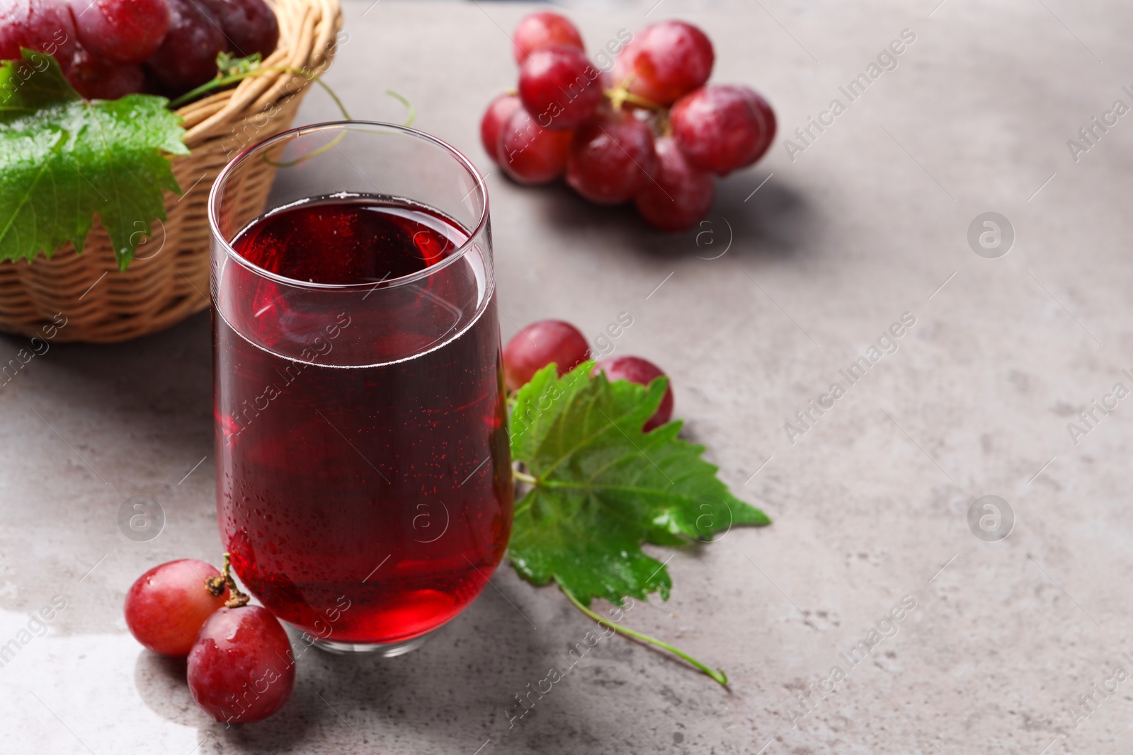 Photo of Ripe grapes and glass of tasty juice on grey table