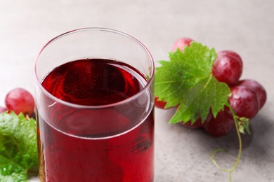 Ripe grapes and glass of tasty juice on grey table, closeup