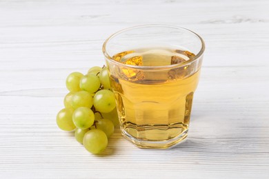 Ripe grapes and glass of tasty juice on white wooden table, closeup