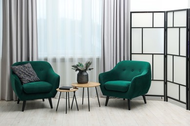 Photo of Comfortable armchairs, coffee table and folding screen near window in living room