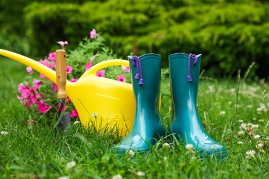 Photo of Rubber boots, gardening tools and petunia flowers on green grass outdoors