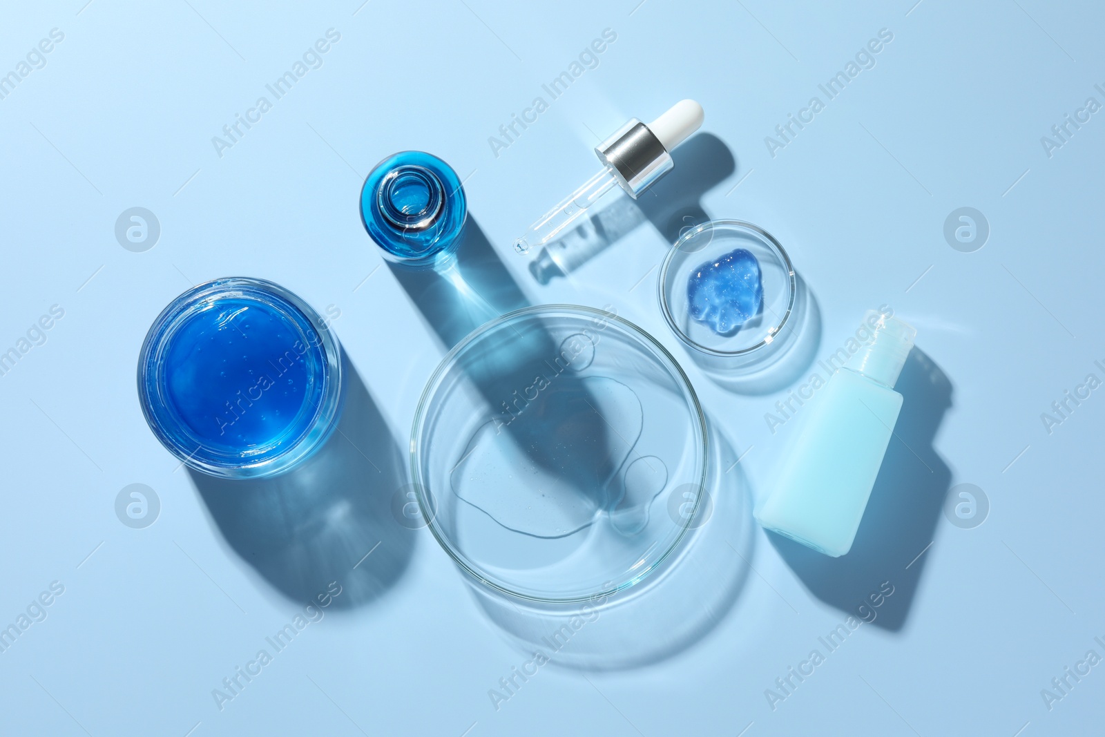 Photo of Petri dishes with cosmetic product and pipette on light blue background, flat lay