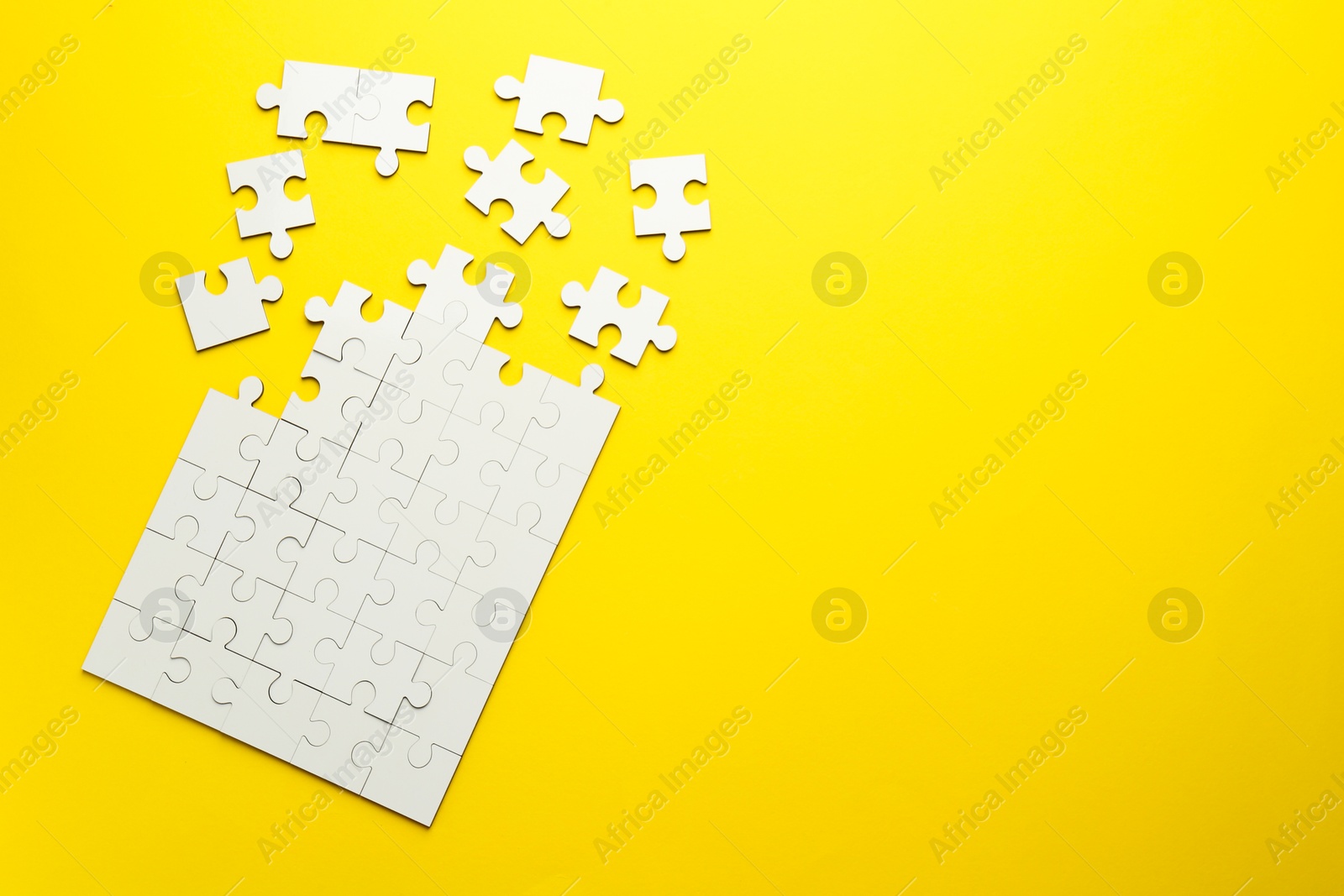 Photo of White puzzle pieces on yellow background, top view. Space for text