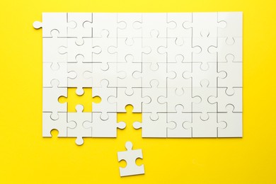 Photo of White puzzle pieces on yellow background, top view