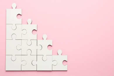 Photo of White puzzle pieces on pink background, top view. Space for text