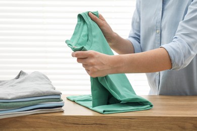 Woman stacking clean clothes at wooden table indoors, closeup