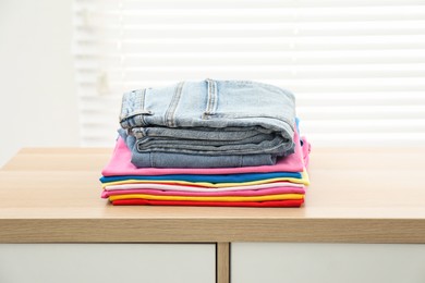 Photo of Stack of clean clothes on wooden dresser indoors