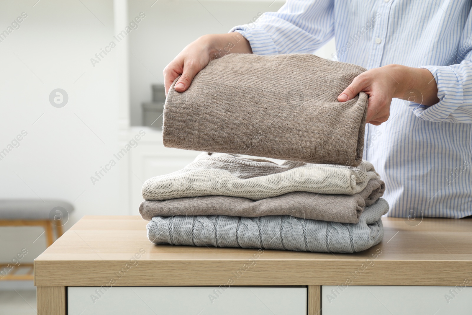 Photo of Woman stacking clean clothes at wooden dresser indoors, closeup