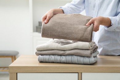 Woman stacking clean clothes at wooden dresser indoors, closeup