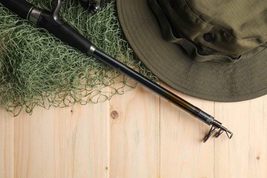 Fishing rod with spinning reel, hat and net on wooden table, top view