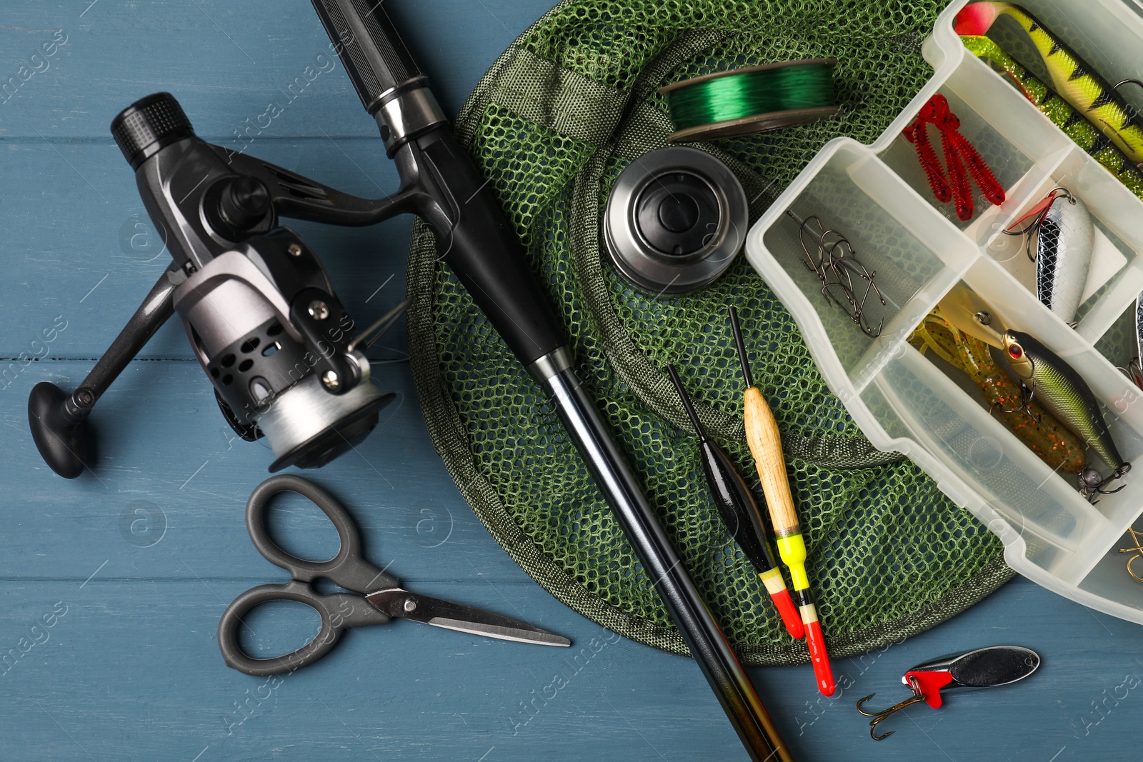 Photo of Fishing rod with spinning reel, baits, floats, scissors, net and line on blue wooden table, top view