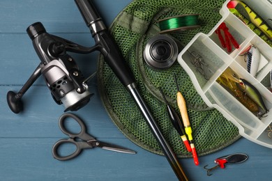 Fishing rod with spinning reel, baits, floats, scissors, net and line on blue wooden table, top view