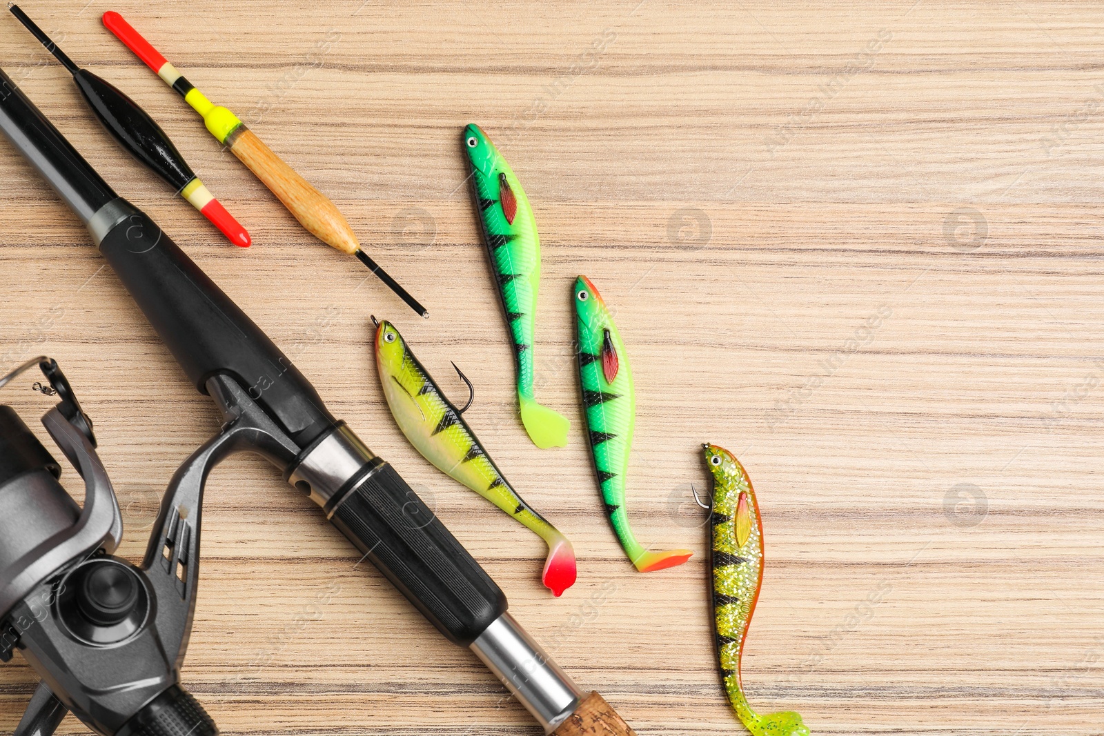 Photo of Fishing rod with spinning reel, baits and floats on wooden table, flat lay. Space for text