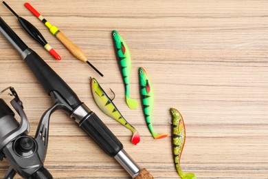 Photo of Fishing rod with spinning reel, baits and floats on wooden table, flat lay. Space for text