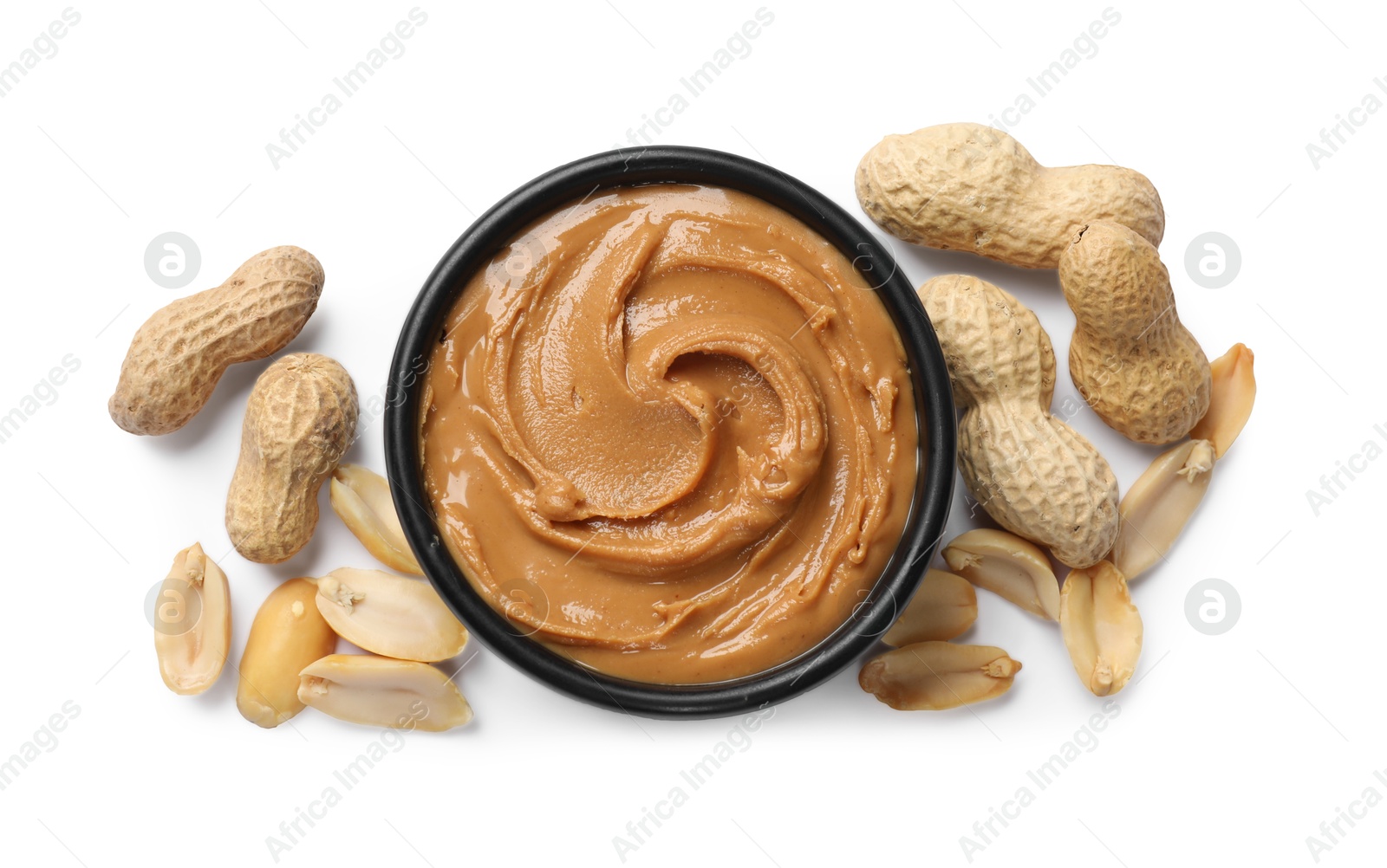 Photo of Tasty peanut butter in bowl and groundnuts isolated on white, top view