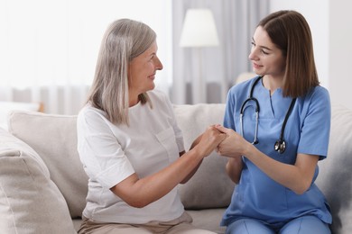 Photo of Smiling healthcare worker supporting senior patient indoors