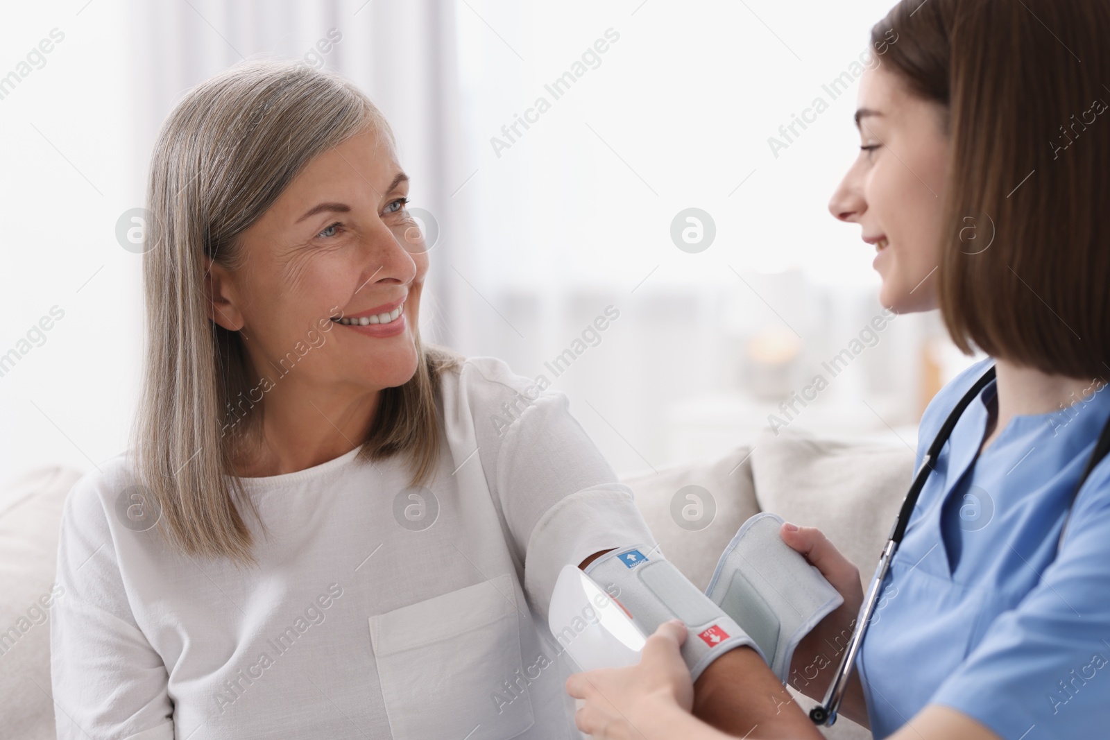 Photo of Young healthcare worker measuring patient's blood pressure indoors