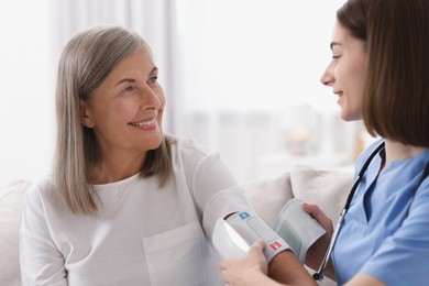 Young healthcare worker measuring patient's blood pressure indoors