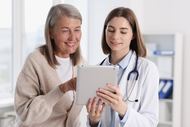 Smiling healthcare worker and senior patient checking analysis results on tablet in hospital