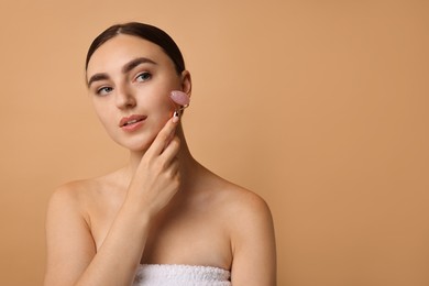 Photo of Beautiful young woman doing facial massage with roller on beige background, space for text