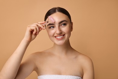 Photo of Beautiful young woman doing facial massage with roller on beige background