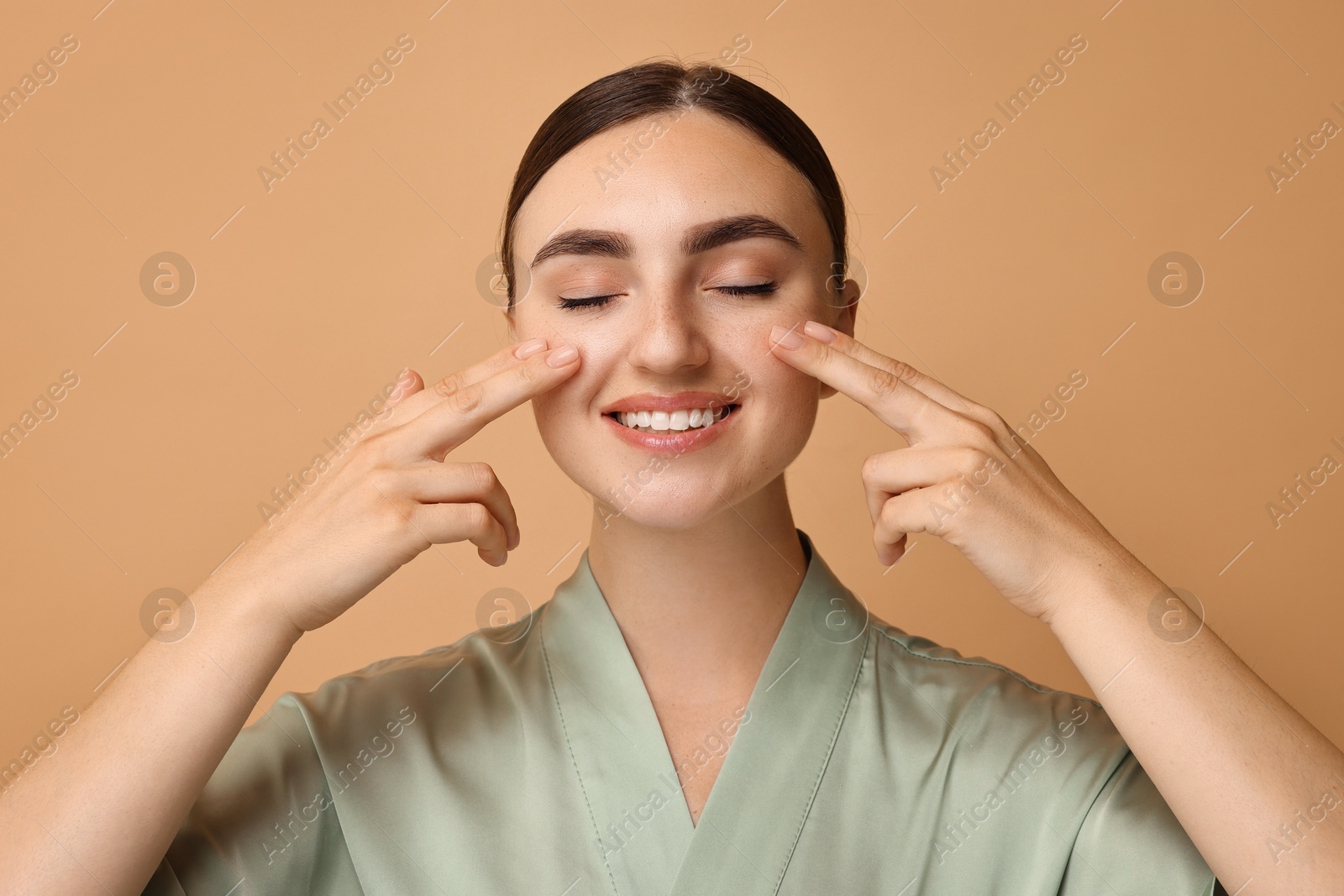 Photo of Face massage. Beautiful young woman with healthy skin on beige background