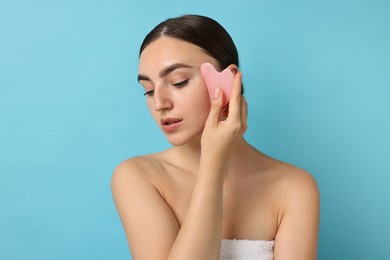 Photo of Beautiful young woman doing facial massage with gua sha tool on light blue background