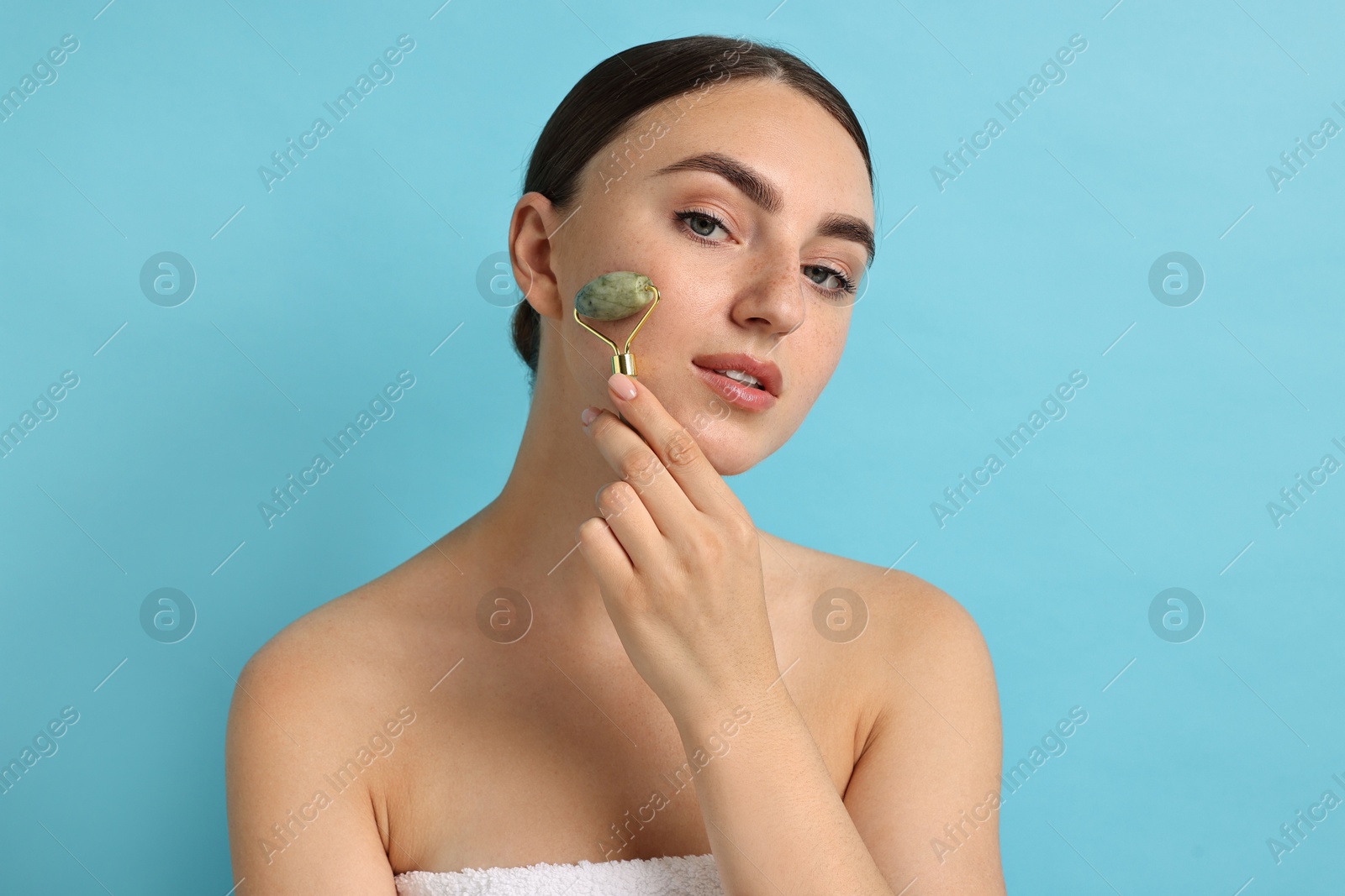 Photo of Beautiful young woman doing facial massage with roller on light blue background