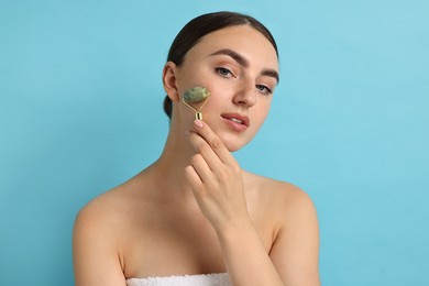 Beautiful young woman doing facial massage with roller on light blue background