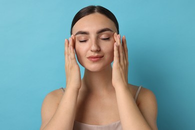 Beautiful young woman doing facial massage on light blue background