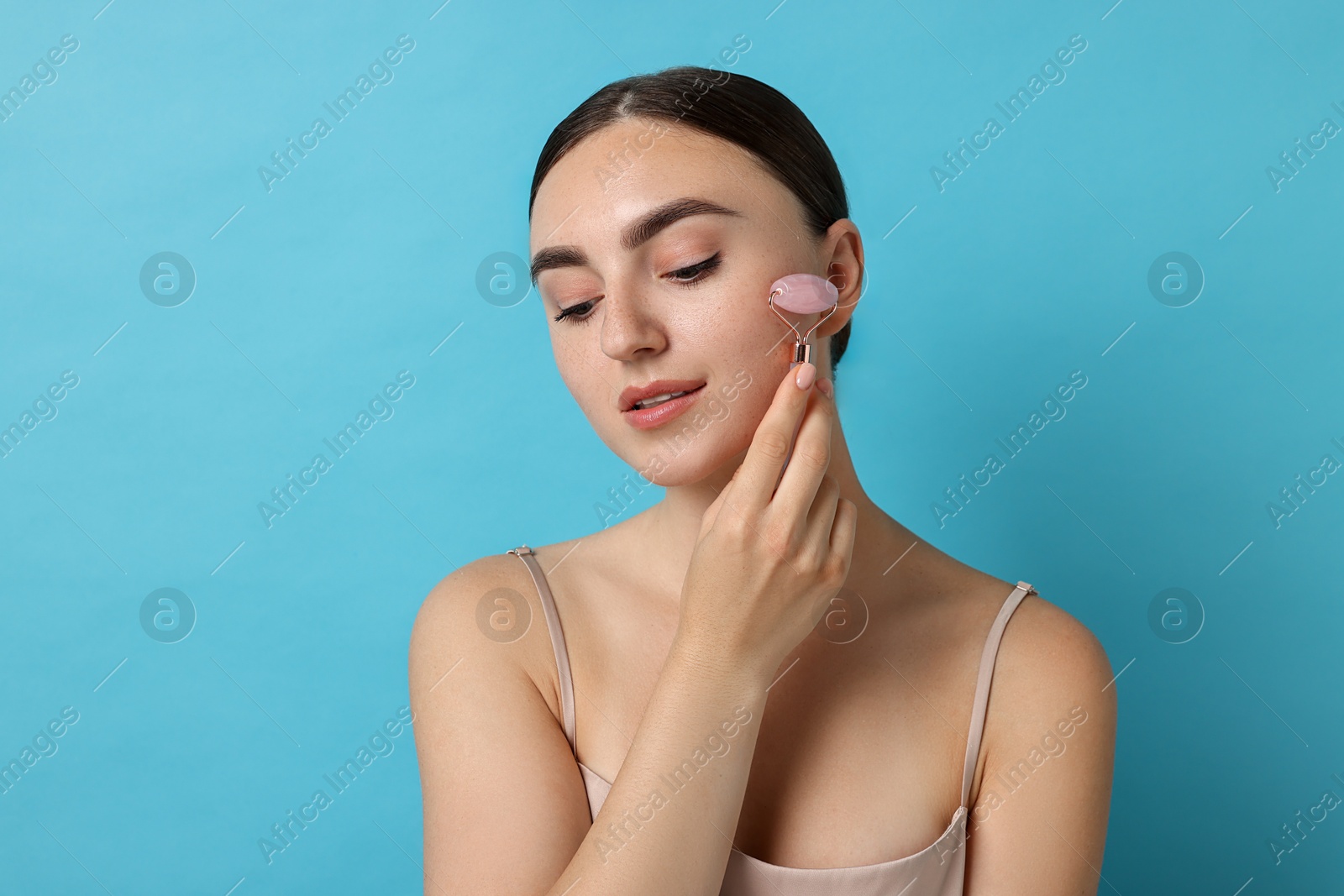 Photo of Beautiful young woman doing facial massage with roller on light blue background