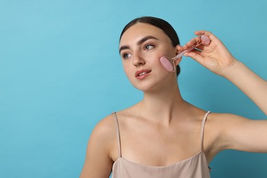 Beautiful young woman doing facial massage with roller on light blue background, space for text